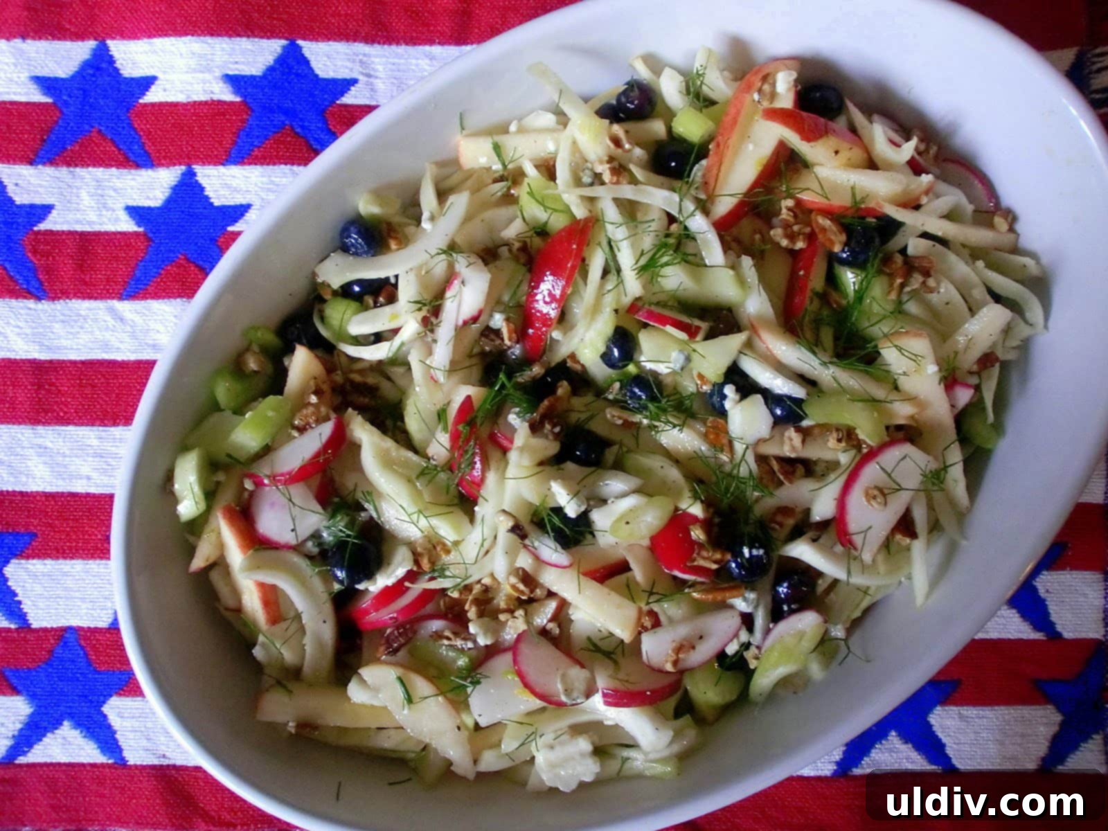 Crisp Apple & Fennel Slaw with Radish, Pecans, and Blue Cheese 9 A serving dish with raw fennel and apple salad, garnished with green fronds and blueberries.
