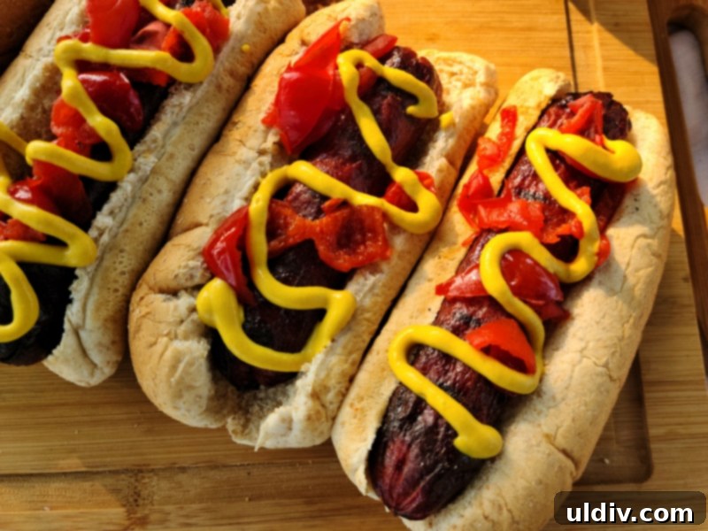 Bison hot dogs artfully arranged with bright Peppadew peppers and a drizzle of mustard, promising a delicious bite.