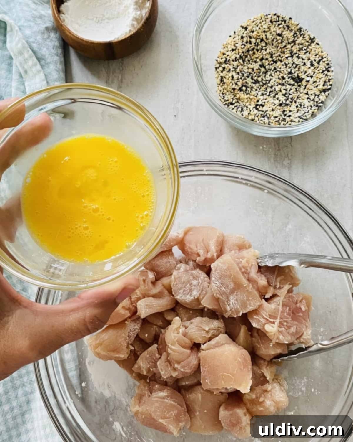 Ultimate Everything Chicken Bites with Fresh Basil Hummus 5 Adding beaten egg to bite-sized chicken pieces in a bowl, ensuring full coverage.