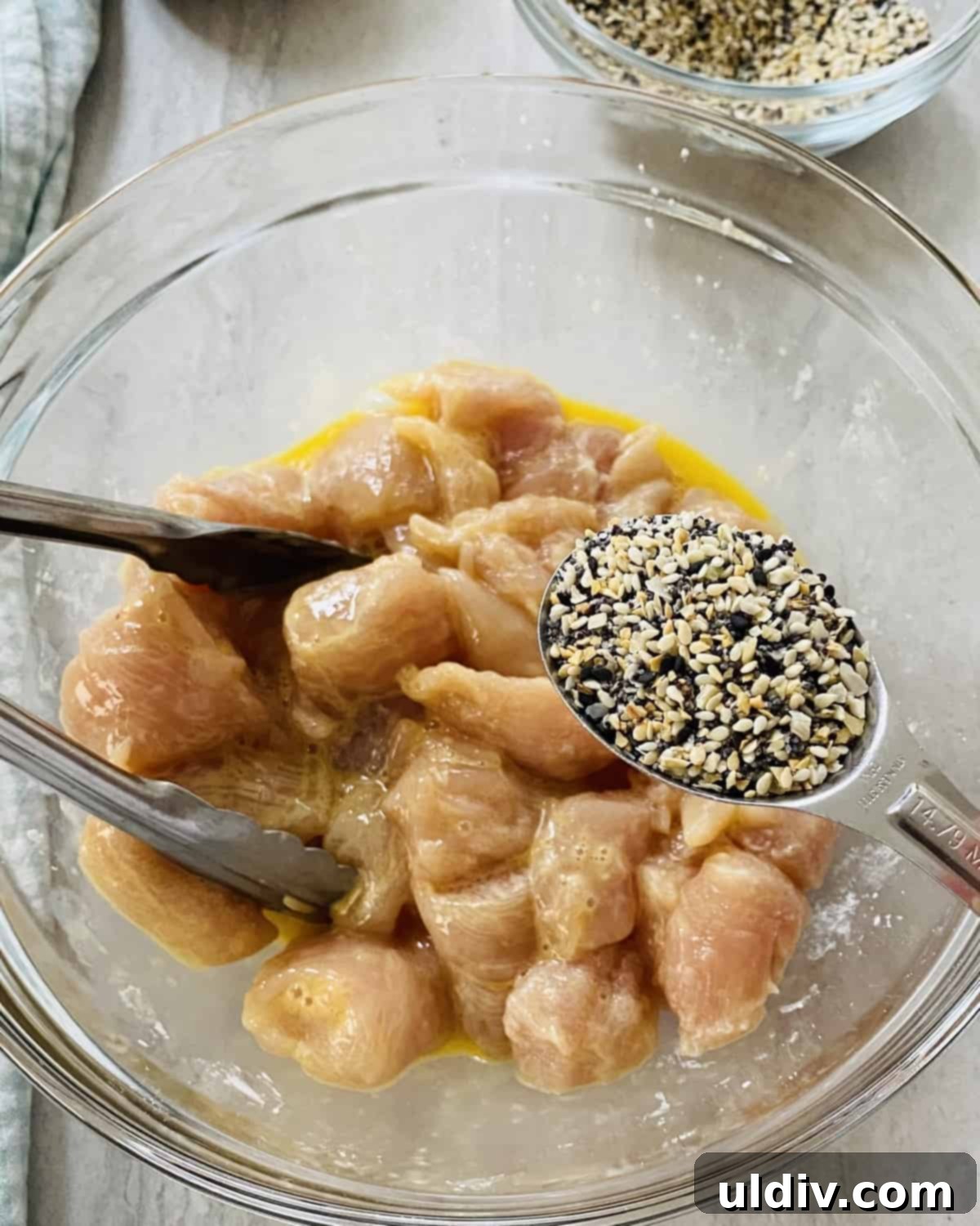 Ultimate Everything Chicken Bites with Fresh Basil Hummus 6 Tossing chicken pieces with Everything But The Bagel spice mix in a bowl, showing generous coating.