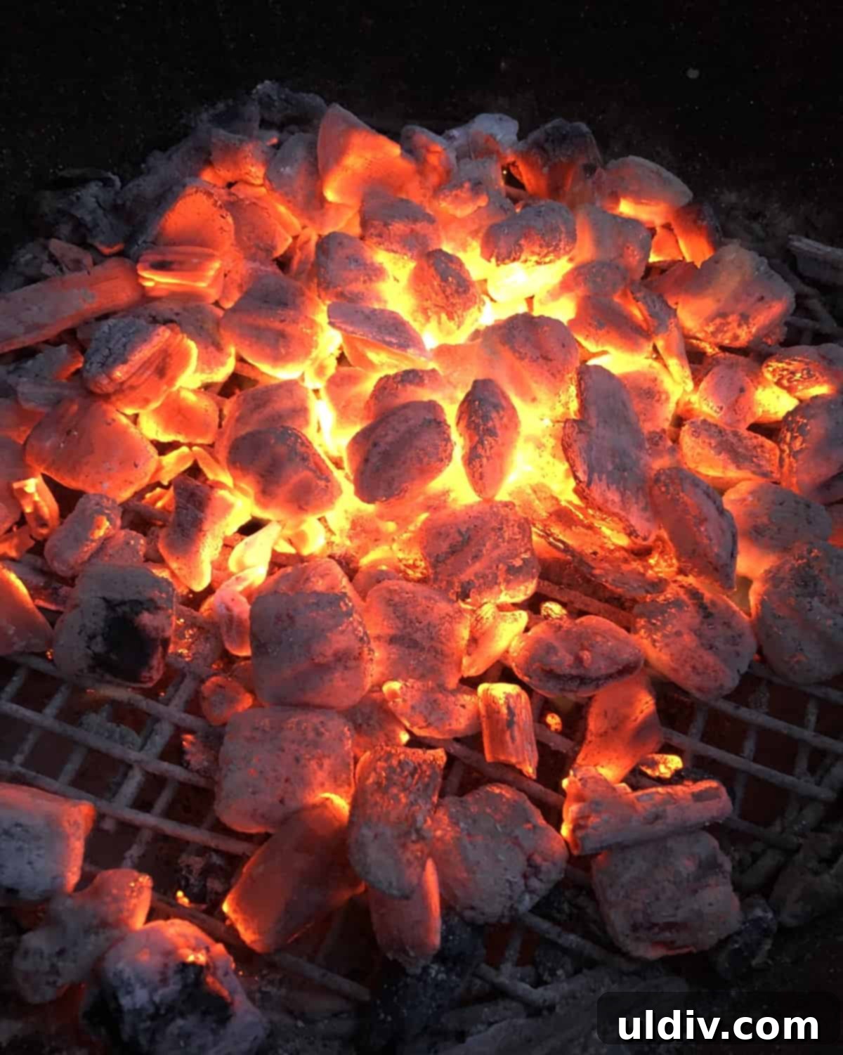 Close-up of glowing red hot charcoal briquettes in a Weber grill, indicating high heat for grilling.