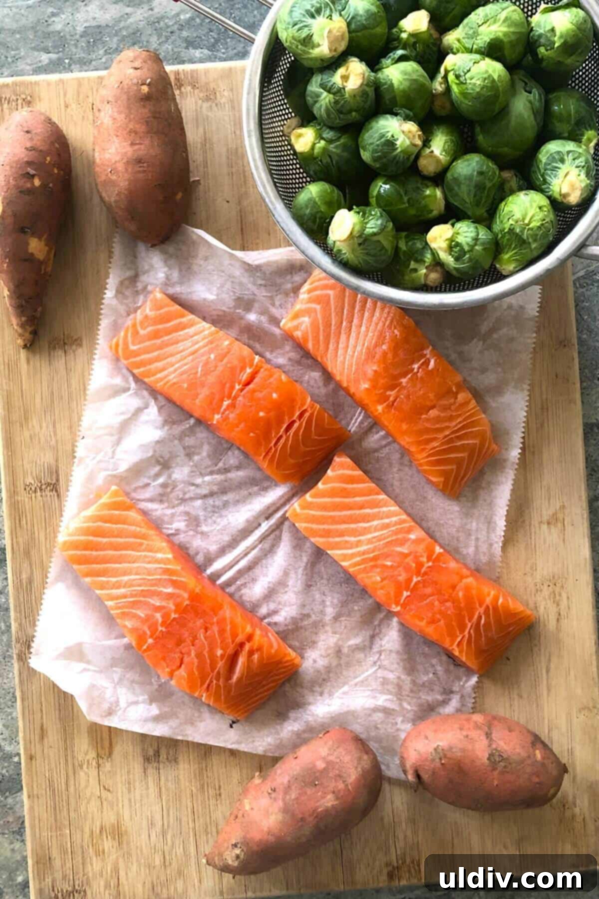 One-Pan Maple Salmon with Roasted Sweet Potatoes and Brussels Sprouts 3 salmon, Brussels sprouts, and sweet potatoes on a cutting board.