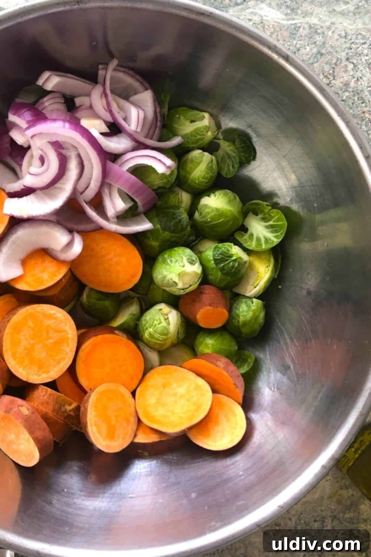 One-Pan Maple Salmon with Roasted Sweet Potatoes and Brussels Sprouts 5 sweet potatoes, Brussels sprouts, red onion in a metal bowl.