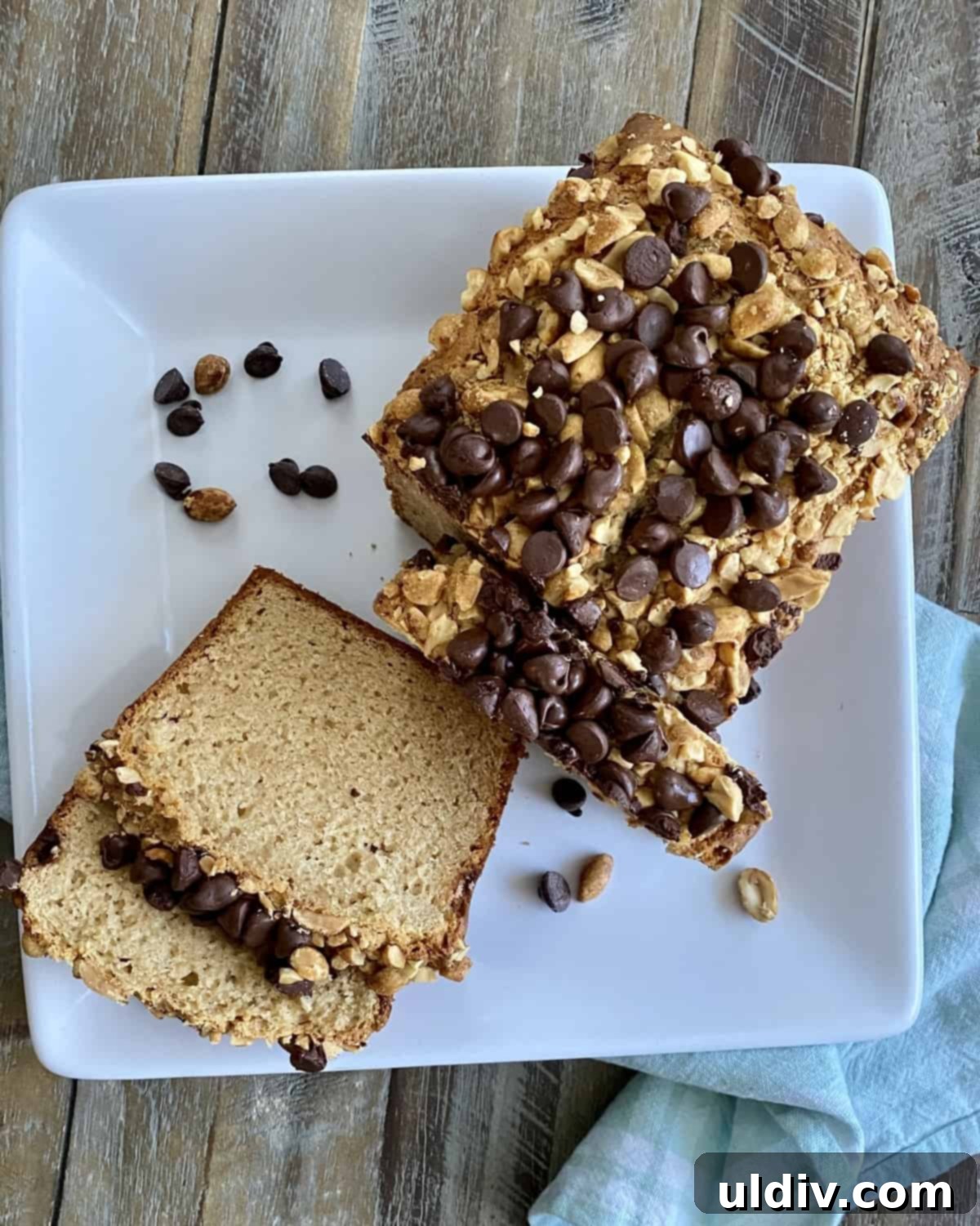 Double Peanut Chocolate Chip Loaf 2 Two slices of moist peanut butter bread next to a half-eaten loaf, garnished with chocolate chips and peanuts.
