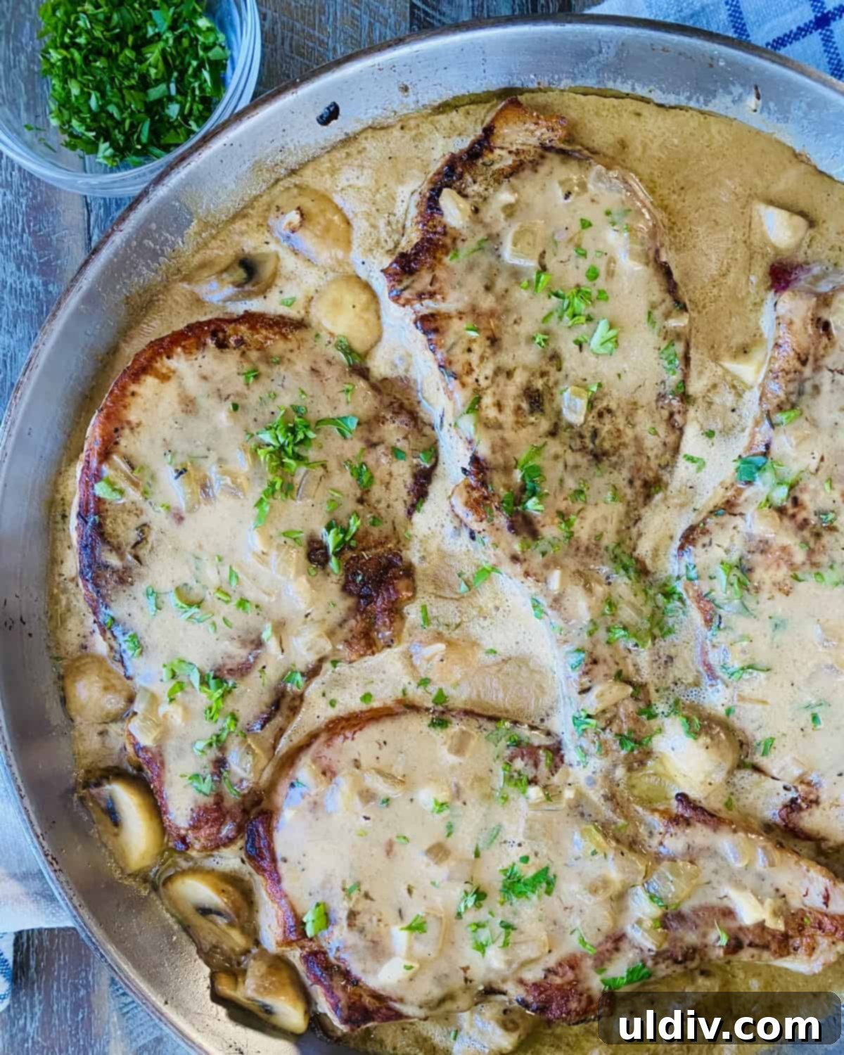Braised Pork Chops with Savory Mushroom Sauce 2 3 bone-in pork chops in mushroom gravy in a sauté pan.