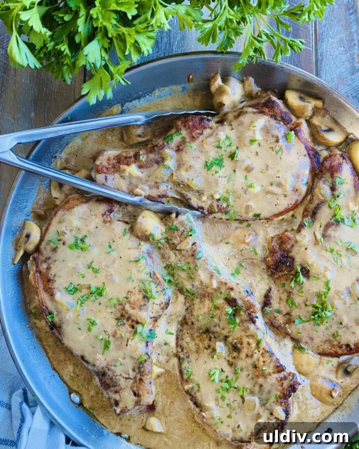 Golden Pork Chops Smothered in Creamy Mushroom Gravy 10 A pan of smothered pork chops with mushroom gravy and a pair of tongs.