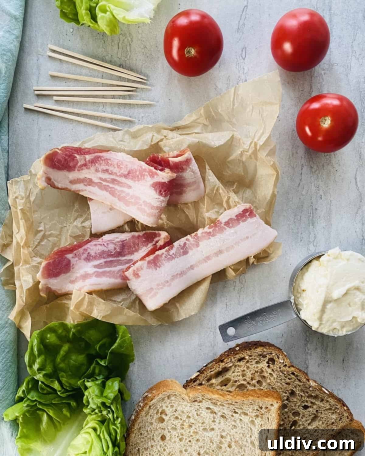 Mini BLT Sandwiches 3 Bacon, tomatoes, lettuce, mayonnaise and slices of bread on a marble board.
