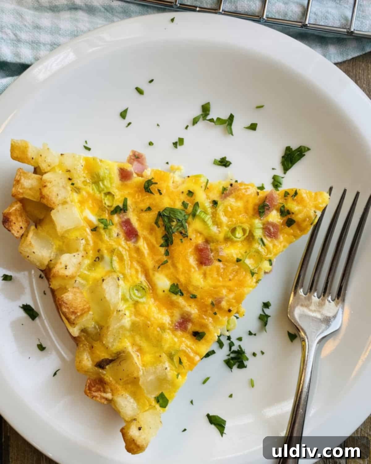 Crispy Hash Brown Quiche with Savory Ham and Cheese 9 A perfectly portioned slice of hash brown crust quiche on a white plate with a fork, ready to be enjoyed as a savory breakfast or brunch.