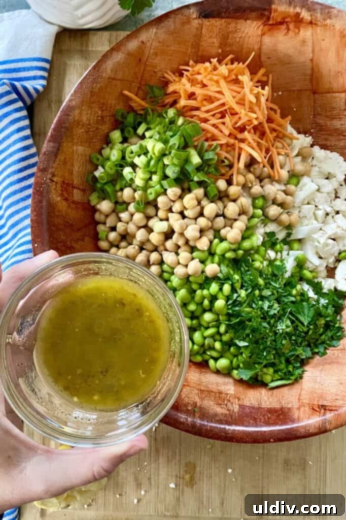 Wholesome Cauliflower Edamame Chickpea Salad 7 pouring vinaigrette over vegetables for cauliflower salad