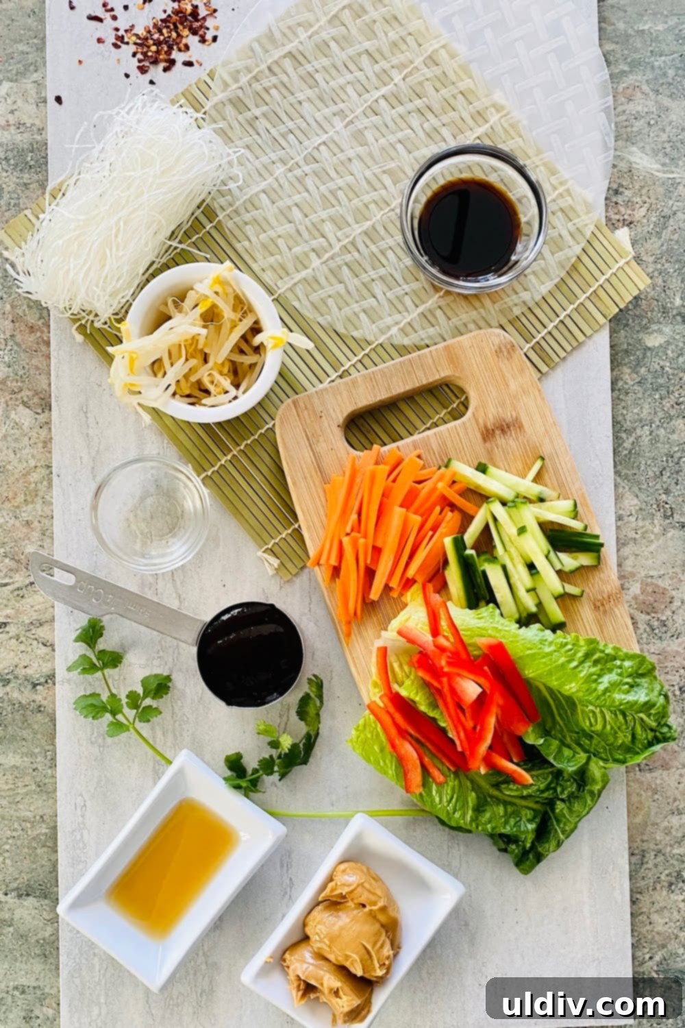 A vibrant assortment of ingredients for spring rolls, including bean sprouts, spring roll wrappers, carrots, cucumbers, and lettuce, laid out on a rolling mat, ready for assembly.