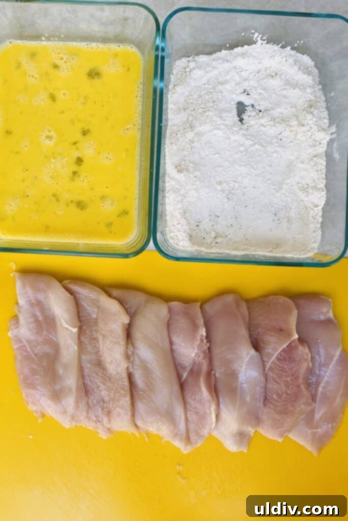 Chicken cutlets seasoned with flour, alongside beaten eggs, laid out on a kitchen counter for dredging.