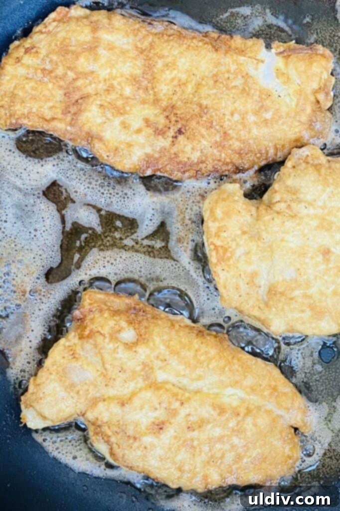 Battered chicken cutlets sizzling and turning golden brown in a hot skillet with oil.