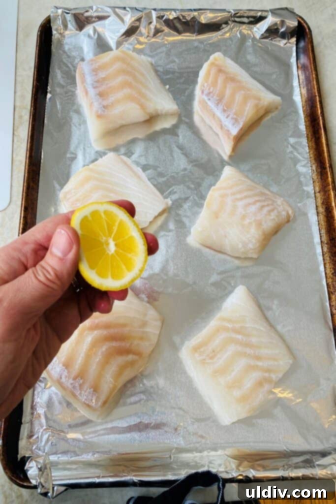Baked Cod with Herbed Breadcrumbs 4 A hand squeezing fresh lemon juice over raw cod fillets on a baking sheet, preparing them for seasoning.