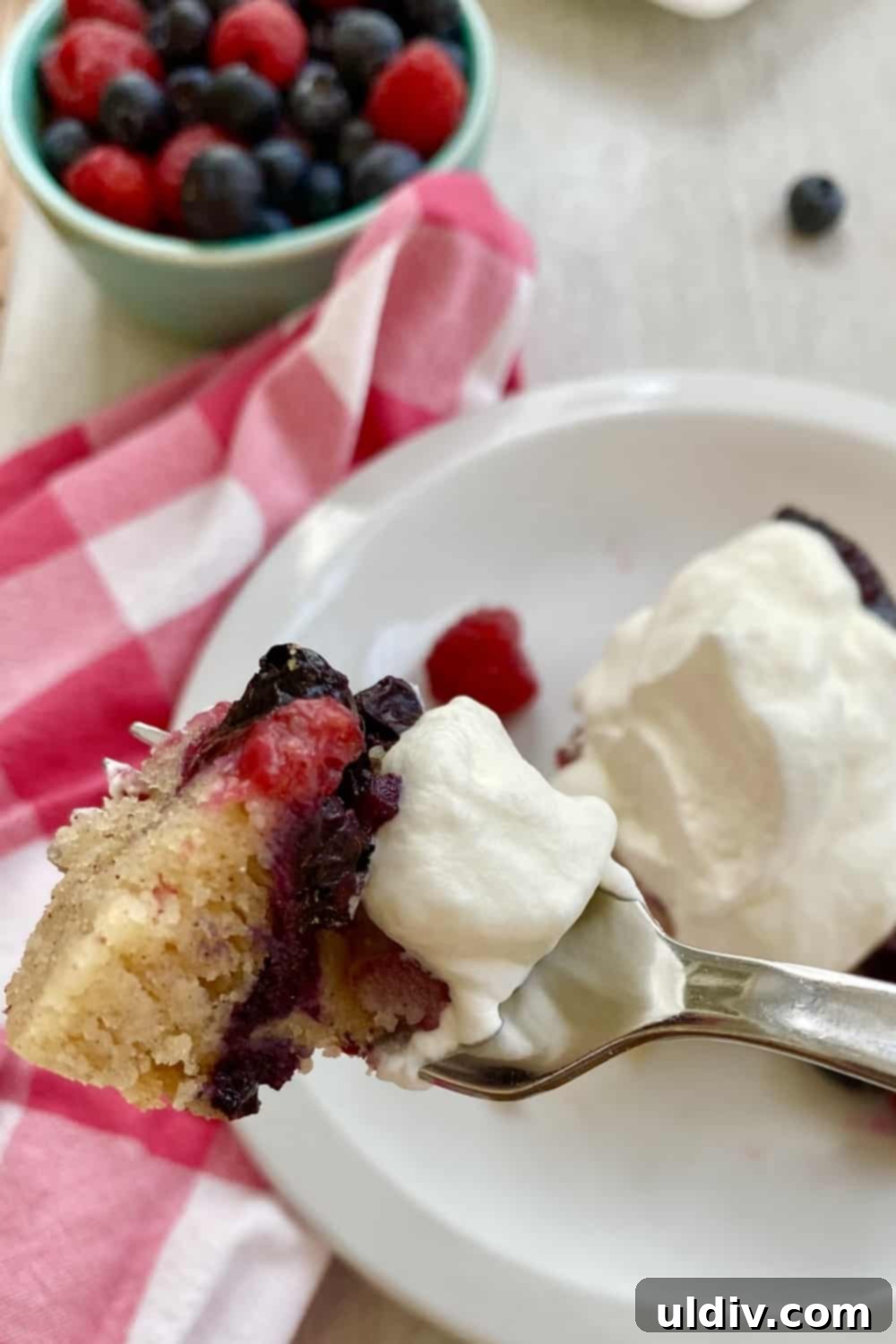 Berry Burst Upside Down Cake 10 A fork taking a bite of berry cake with whipped cream, showing the rich berry layer.