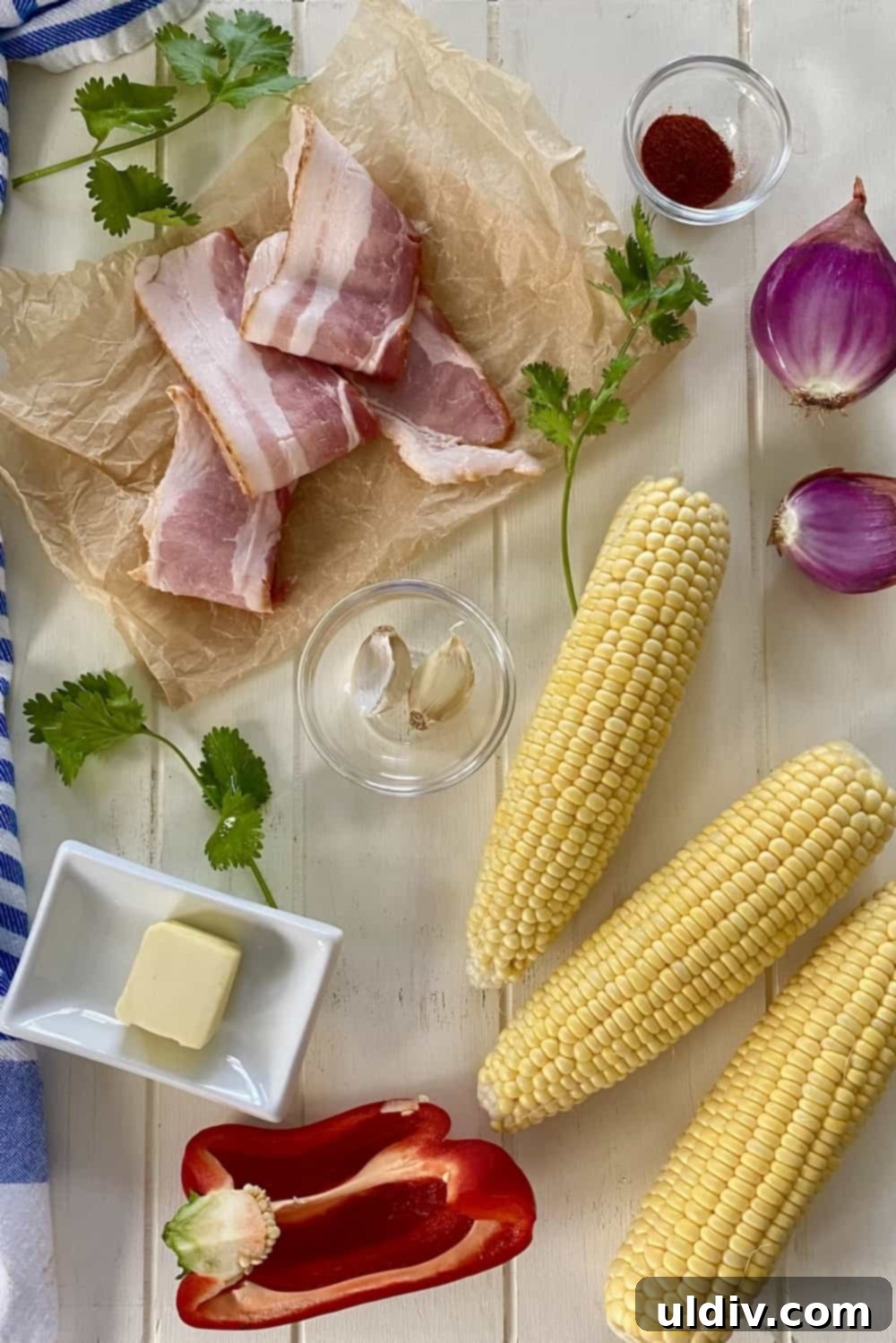 Fresh ingredients laid out for sweet corn salad: corn on the cob, slices of thick-cut bacon, shallots, red bell pepper, and a pat of butter, illustrating the quality needed for the recipe.