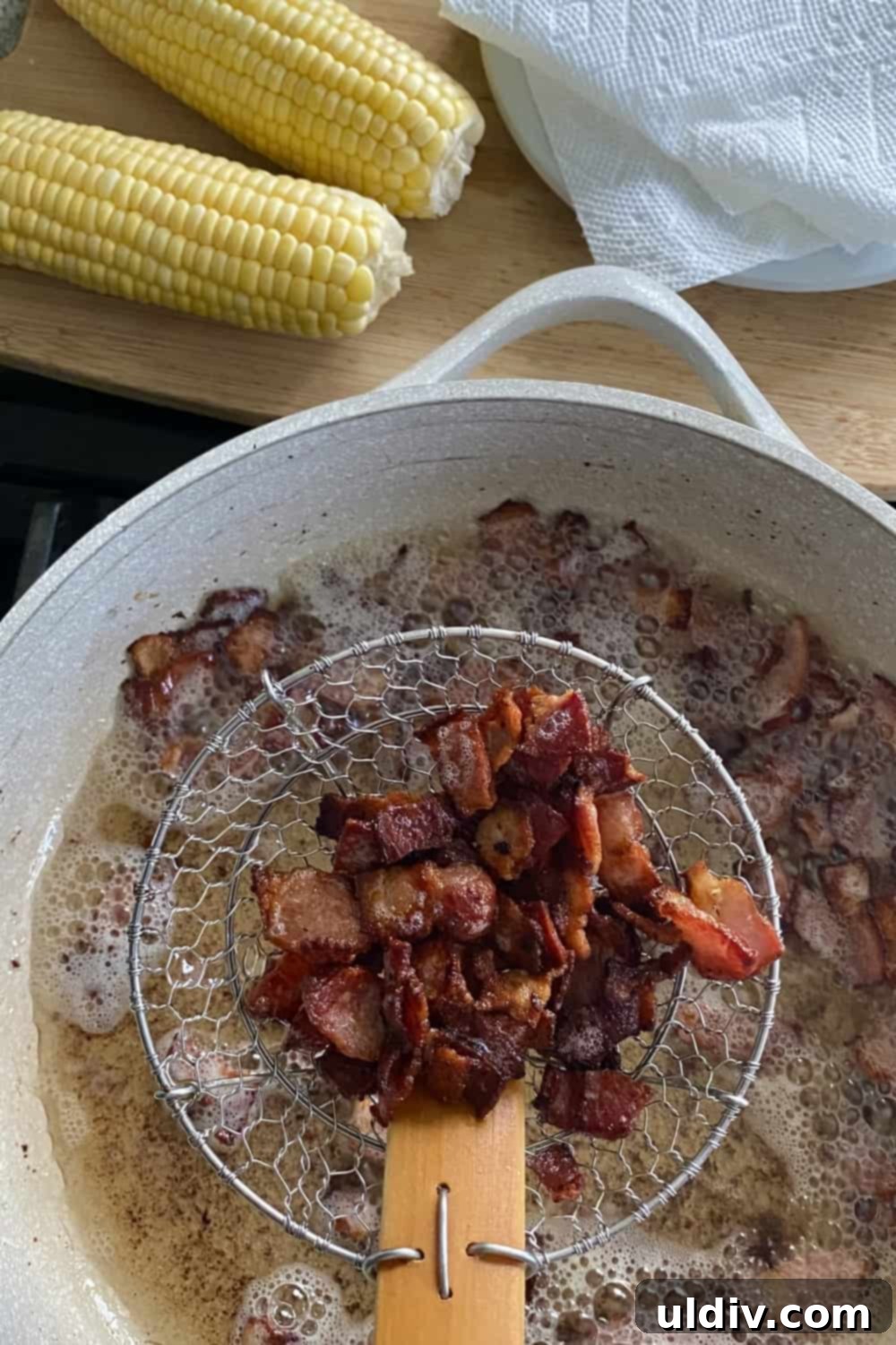 Crispy cooked bacon pieces draining in a strainer basket, ready to be added to the sweet corn salad mixture.