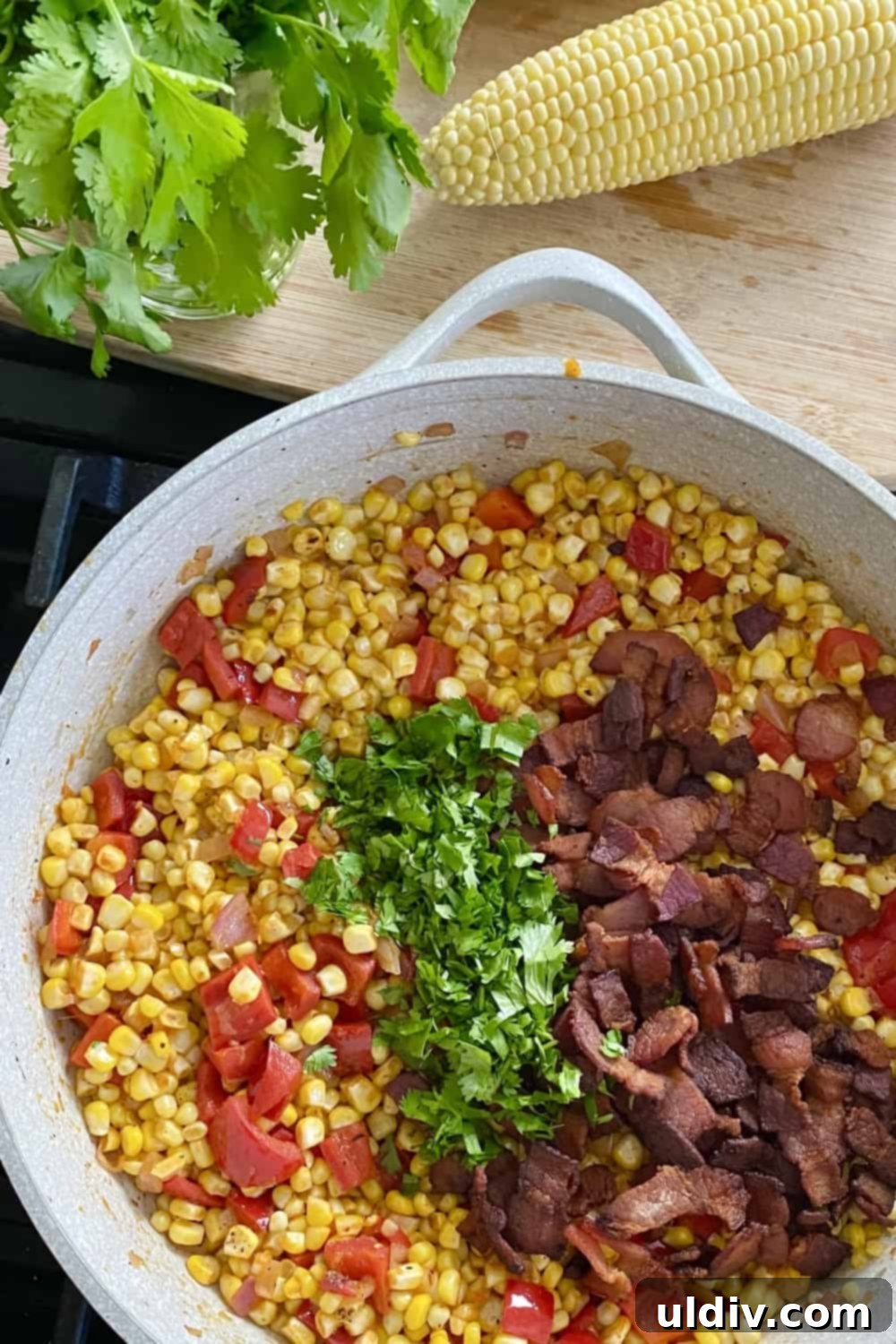Freshly chopped basil and cilantro being added to the warm sweet corn salad, ready to be tossed for a vibrant, aromatic finish.