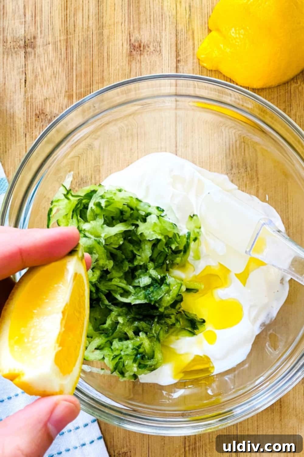 Effortless Tzatziki Dip and Dressing 5 A hand squeezing fresh lemon juice into a bowl containing Greek yogurt and shredded cucumber, adding the essential tang to the tzatziki.
