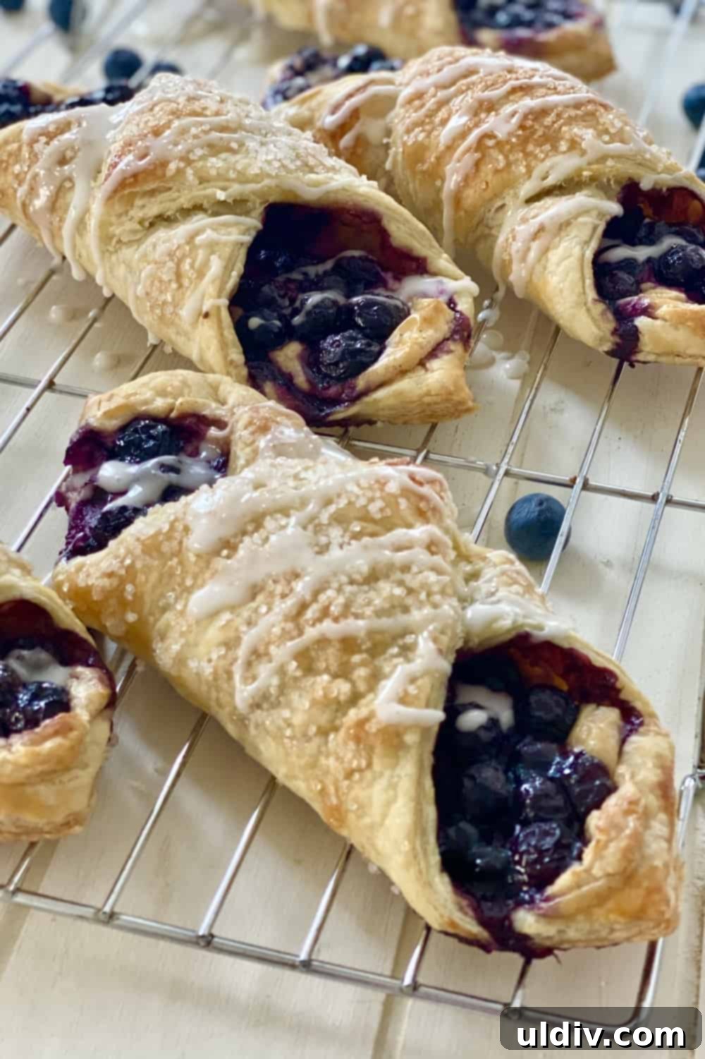 Blueberry Cream Cheese Danish Bliss 3 Freshly baked blueberry danishes cooling on a wire rack, sprinkled with coarse sugar.