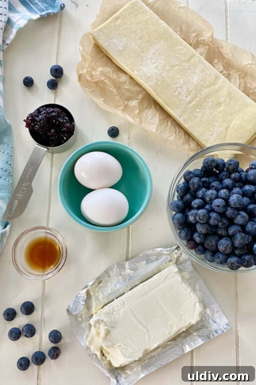 Blueberry Cream Cheese Danish Bliss 4 Ingredients laid out for blueberry danish: cream cheese, eggs, vanilla, blueberries, preserves, and puff pastry.