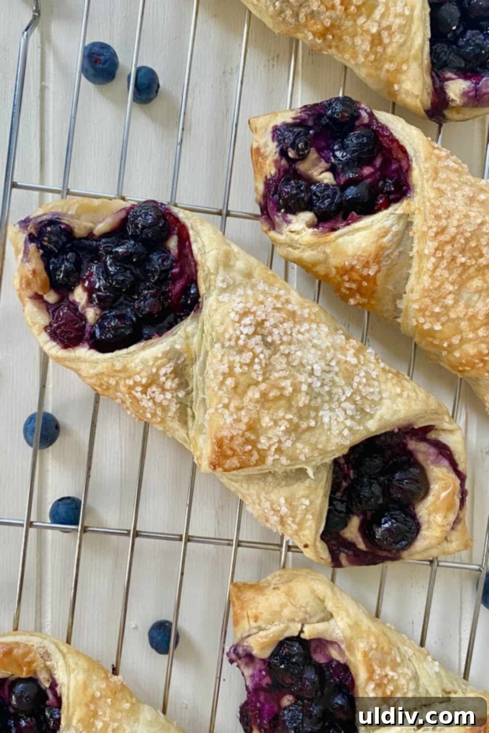 Blueberry Cream Cheese Danish Bliss 9 Two iced blueberry danishes resting on a cooling rack, showcasing their flaky crust and sweet topping.