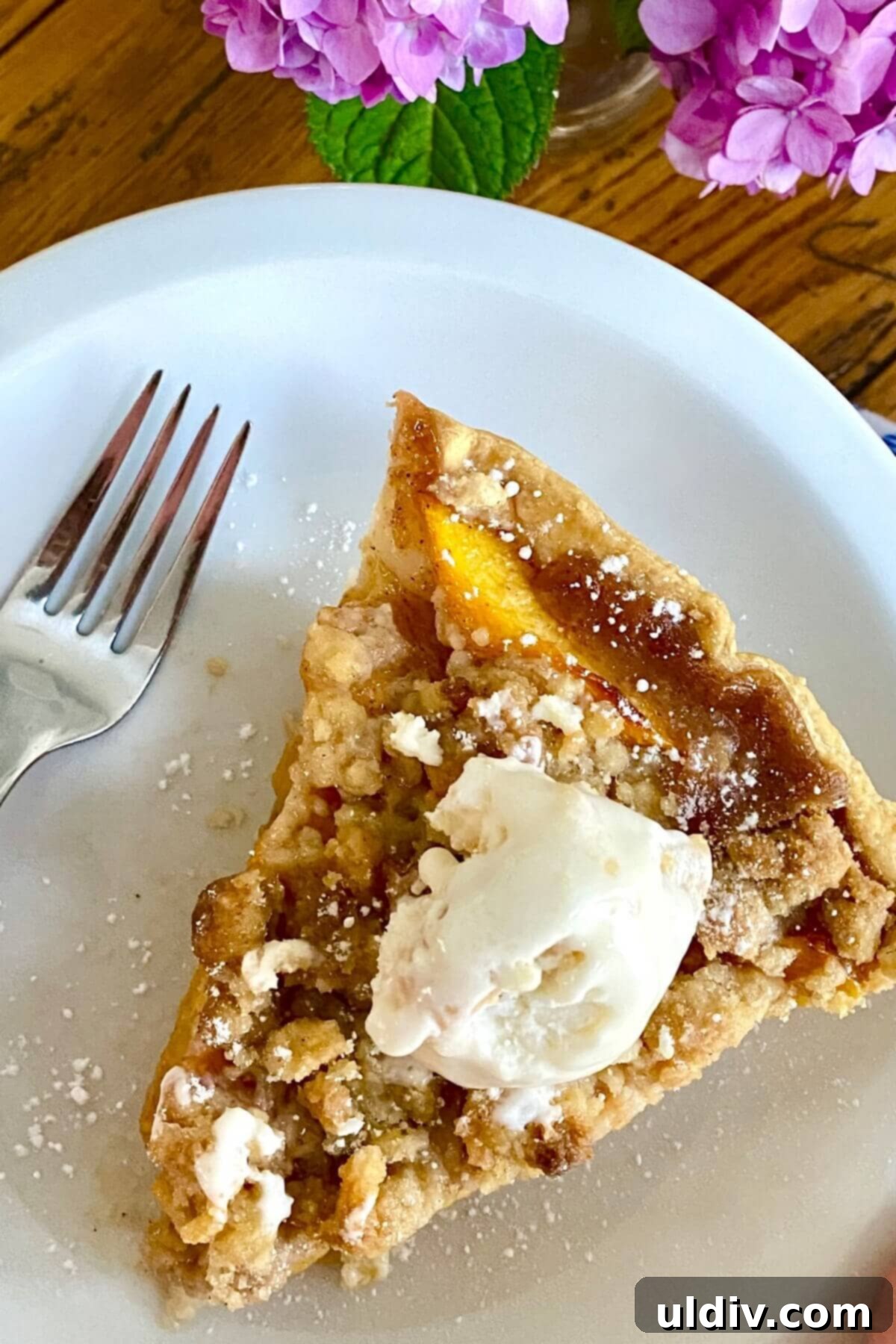 Crisp Bottom Peach Crumble Pie 2 A slice of peach crumble pie on a white plate, showing the golden crust and juicy filling.