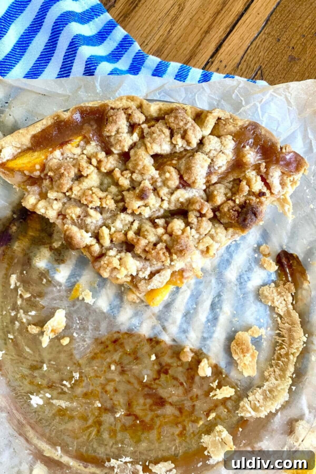 Crisp Bottom Peach Crumble Pie 12 A generous slice of peach crumb pie in a pie plate, ready to be enjoyed.