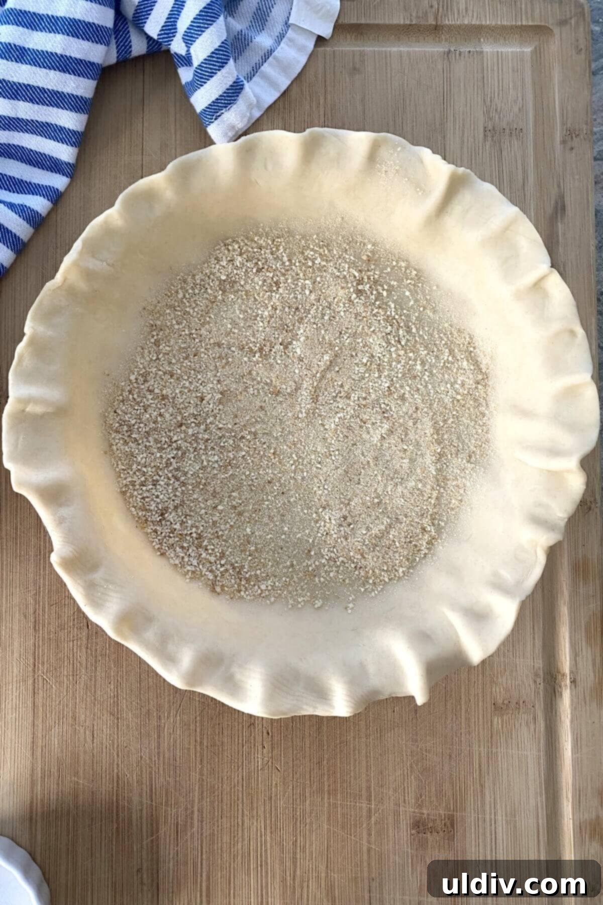 Perfect Peach Crumble Pie 6 An unbaked pie crust expertly placed in a pie plate, with a thin, even layer of dry breadcrumbs sprinkled across its bottom surface.