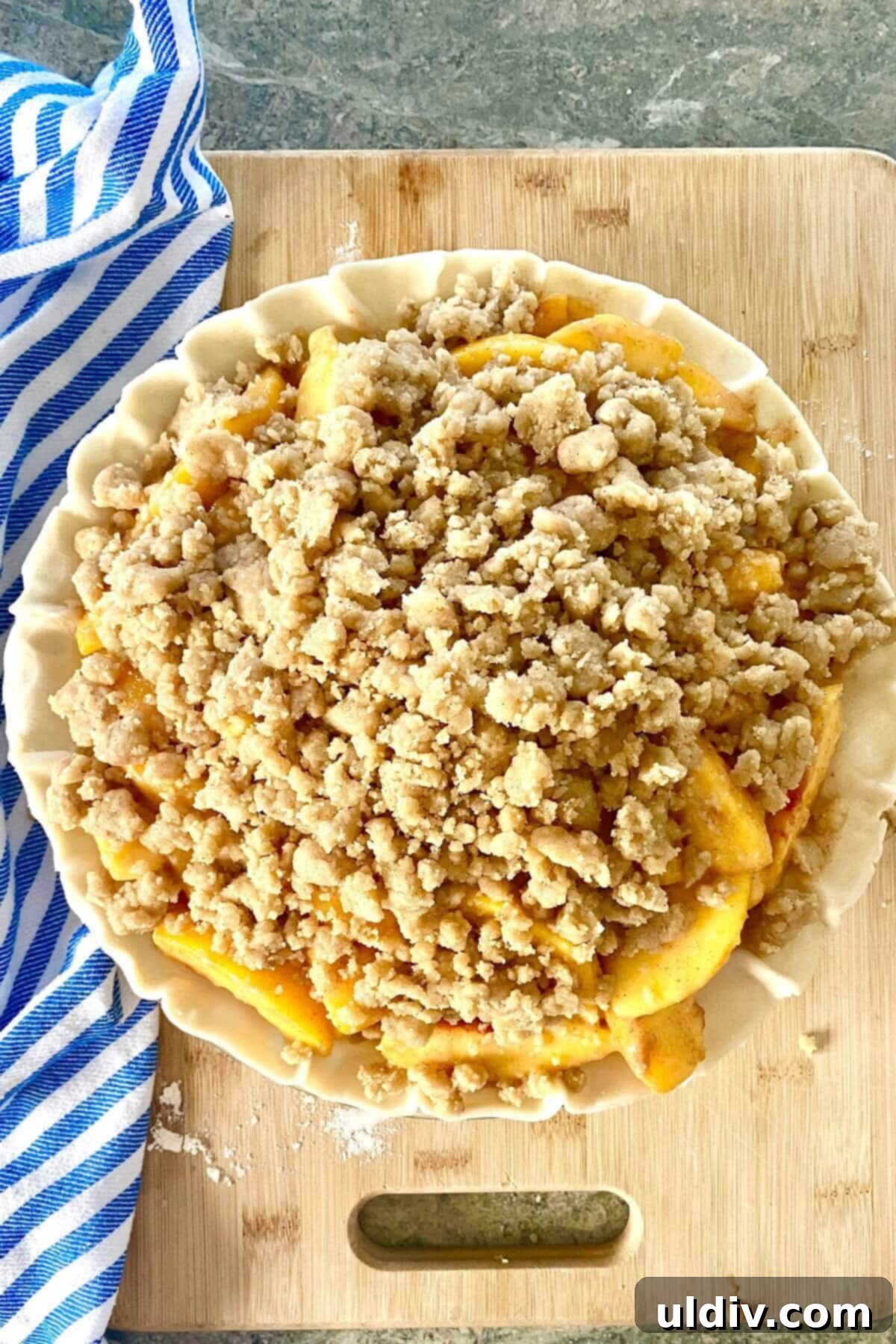 Perfect Peach Crumble Pie 10 An unbaked peach crumble pie with the crumb topping generously sprinkled over the peach filling, ready for the oven.