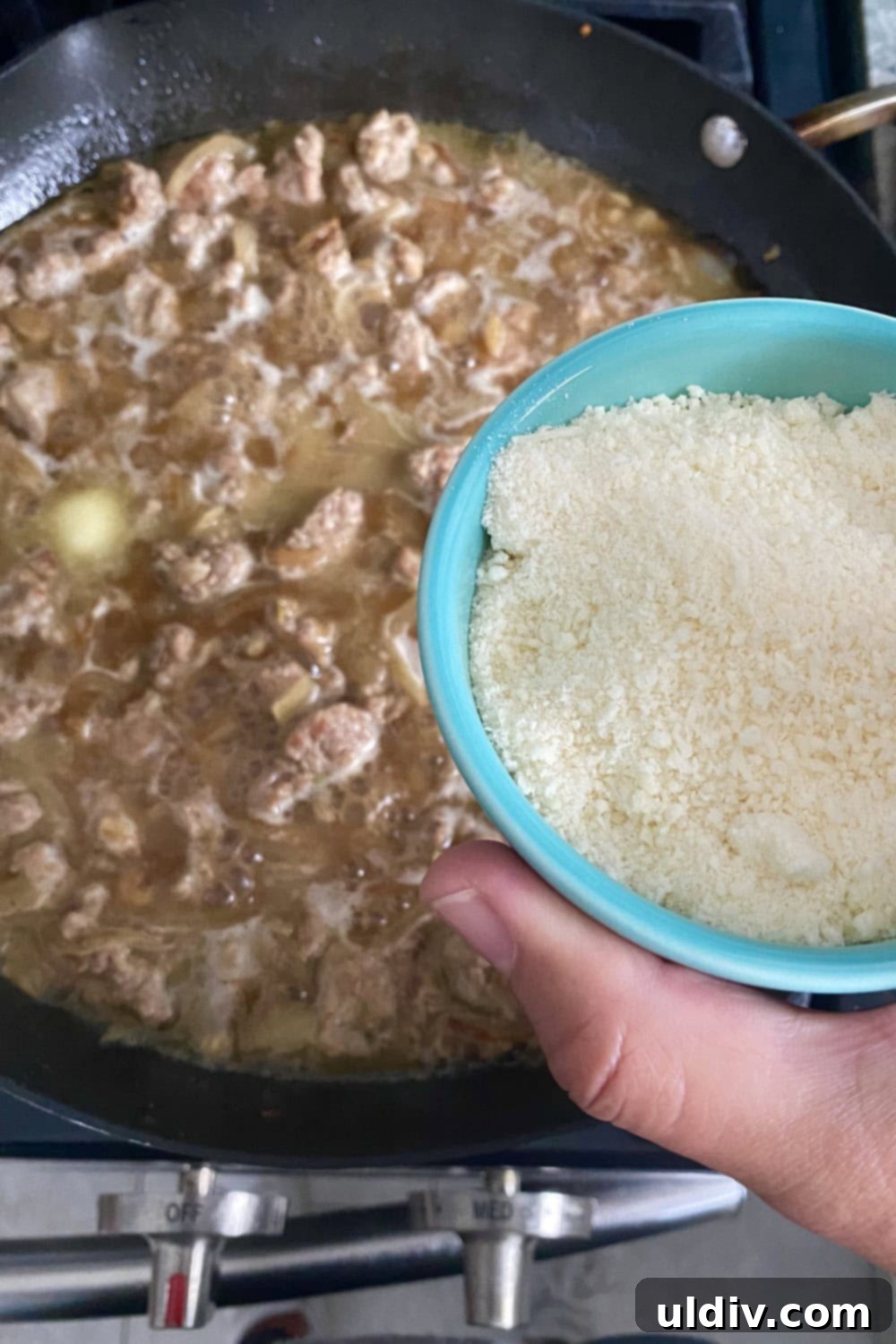 30-Minute Sausage and Pea Pasta 6 Adding grated parmesan cheese to a sausage sauce in a pan.
