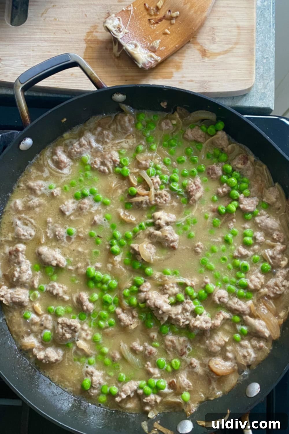 30-Minute Sausage and Pea Pasta 7 A sauté pan with peas, sausage and onion sauce on the stovetop.