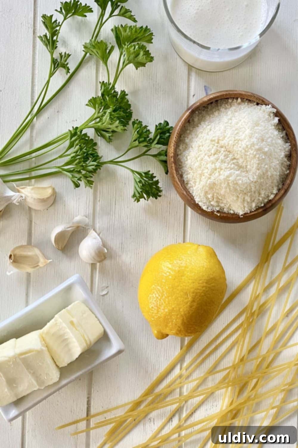 Creamy Garlic Parmesan Noodles 4 Essential ingredients for Grown Up Buttered Noodles: spaghetti, fresh garlic cloves, rich butter, a vibrant lemon, grated Parmesan cheese, and fresh parsley, neatly arranged.