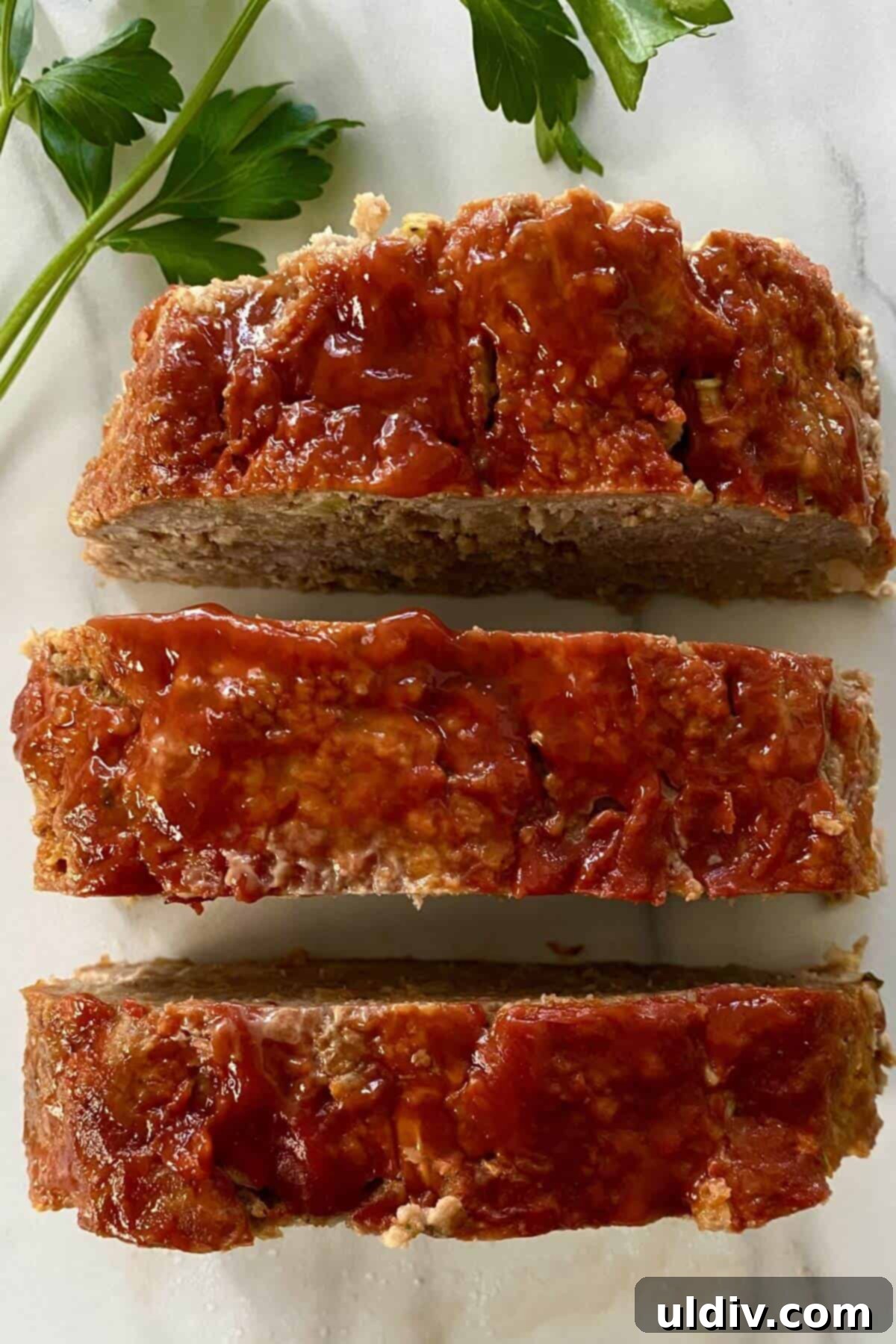 Mom's Legendary Meatloaf Recipe 3 Three perfectly sliced pieces of Mom's Meatloaf, each generously topped with ketchup, ready to be enjoyed.