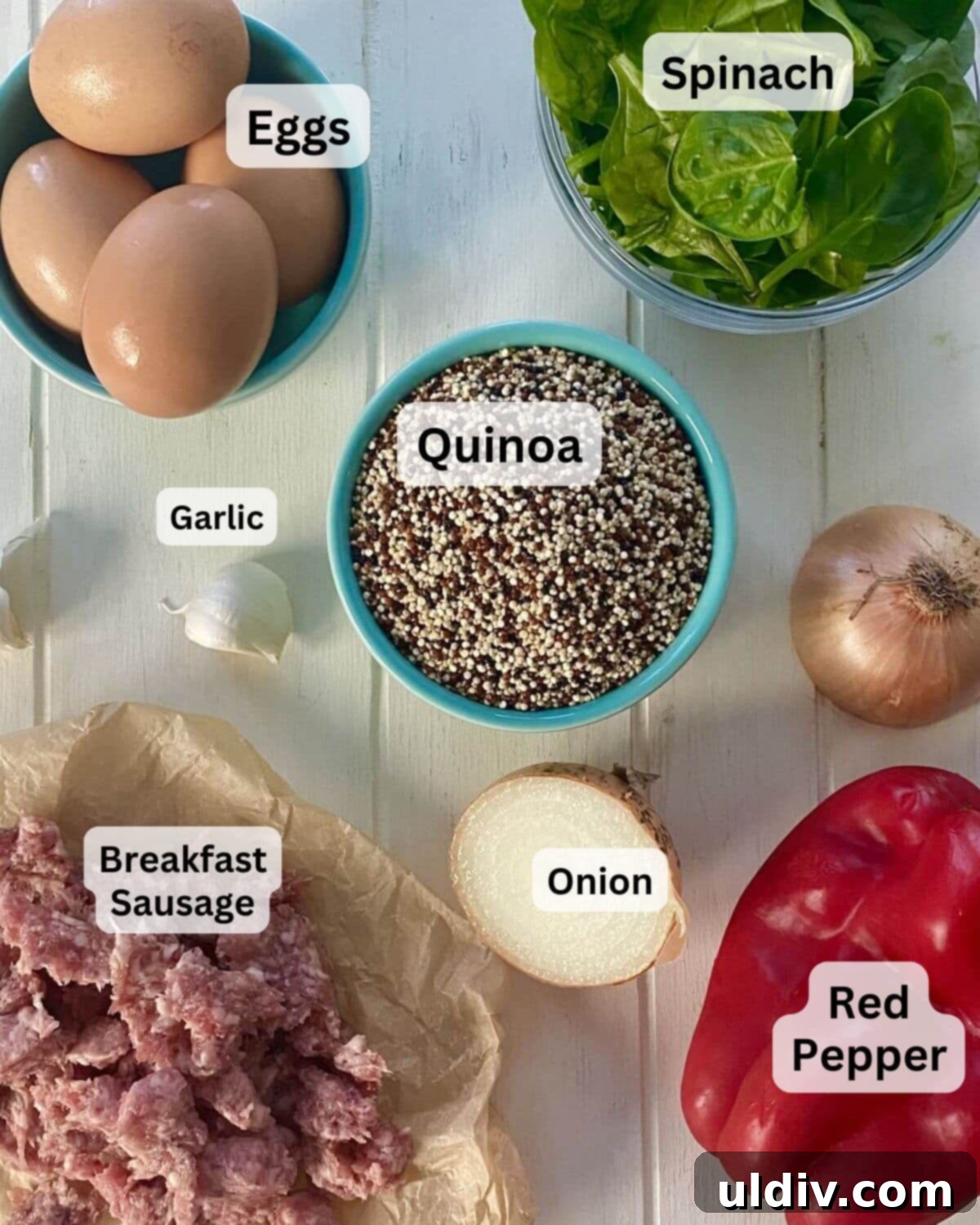 Fuel Your Morning: Savory Quinoa Bowl with Eggs, Sausage & Spinach 3 A collection of fresh ingredients for the quinoa breakfast bowl, including eggs, raw quinoa, breakfast sausage, garlic cloves, fresh spinach, a red onion, and a red bell pepper, neatly arranged on a wooden board.