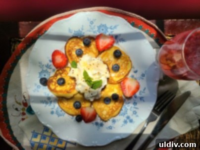 Close-up of a stack of golden-brown lemon ricotta pancakes on a plate with berries and powdered sugar.
