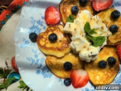 Lemon ricotta pancakes garnished with fresh berries and whipped cream, served with a mocktail next to a window.