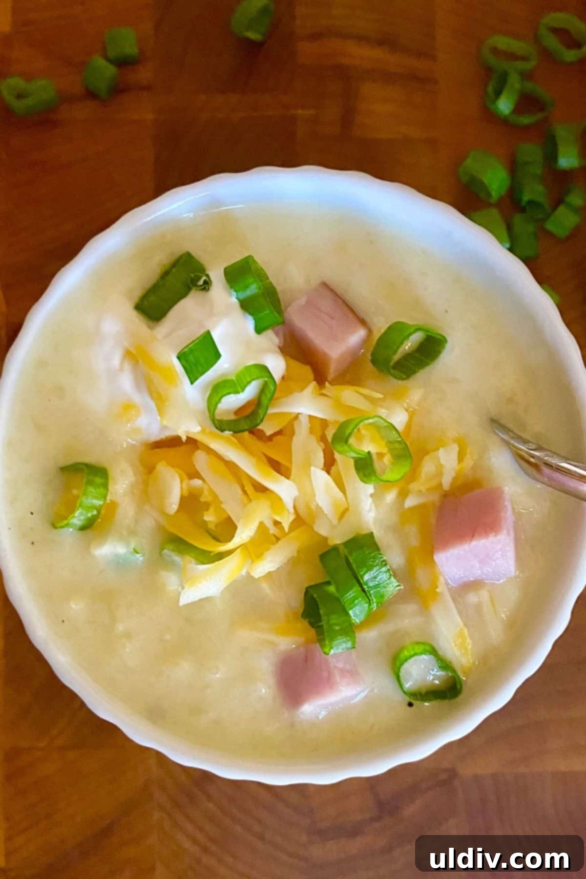 30-Minute Easy Cheesy Ham and Potato Soup 2 A steaming bowl of cheesy ham and potato soup, garnished with sour cream and fresh scallions, promising warmth and comfort.