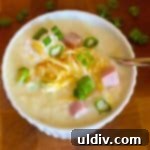 A tantalizing image of cheesy ham and potato soup, garnished with fresh scallions and a dollop of sour cream, ready to be served.