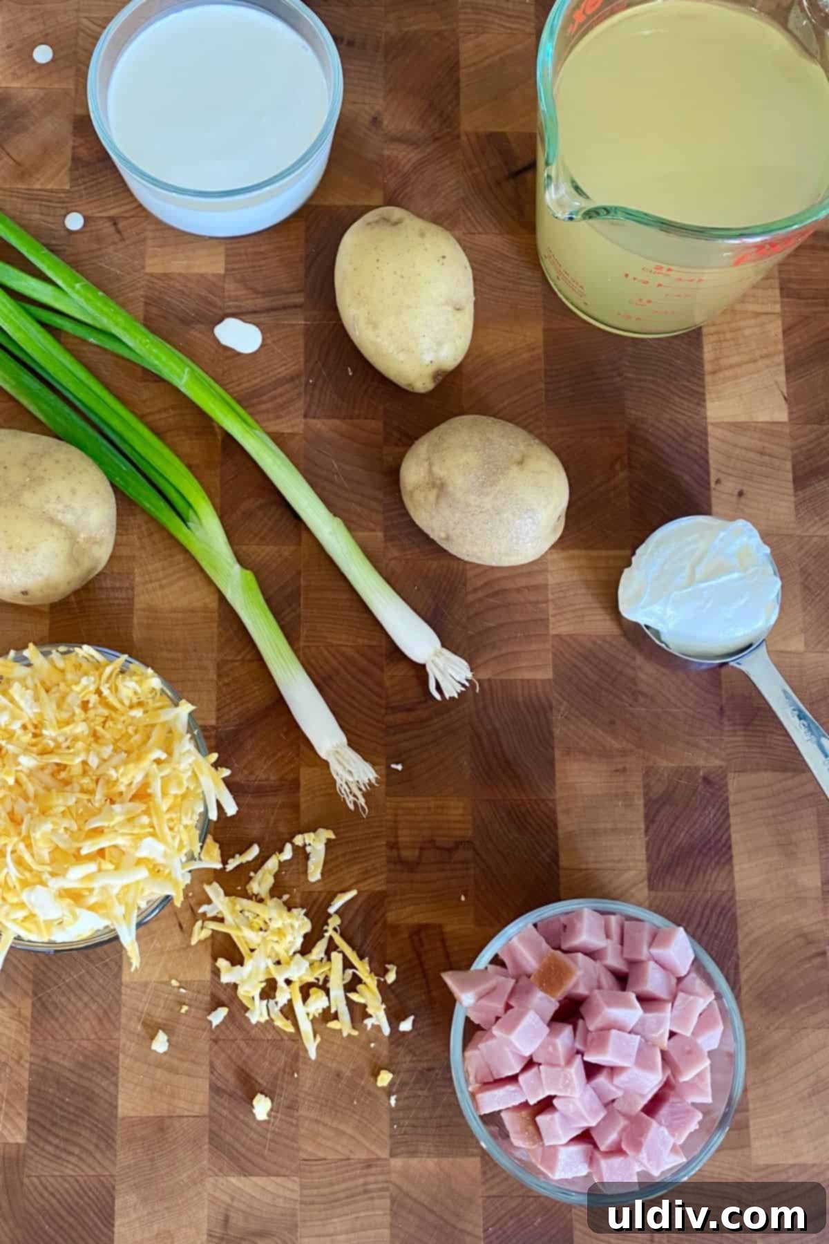 30-Minute Easy Cheesy Ham and Potato Soup 3 A vibrant flat lay of fresh ingredients including diced ham, Yukon Gold potatoes, Colby Jack cheese, chopped scallions, a bowl of chicken stock, sour cream, and heavy cream – all ready for making creamy ham and potato soup.