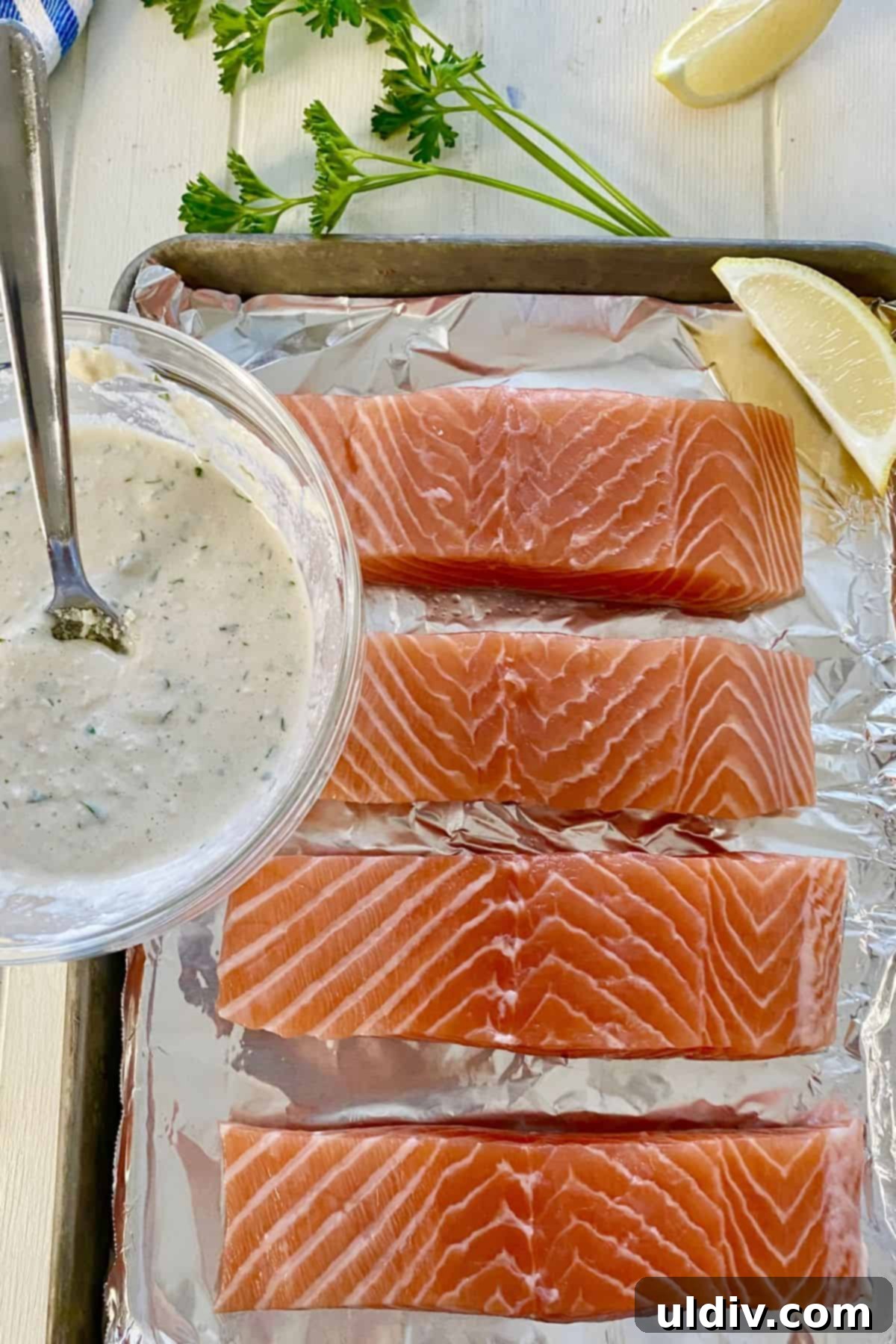 Roasted Salmon Caesar Salad 4 Raw salmon fillets arranged on a foil-lined baking sheet, alongside a bowl of creamy Caesar sauce.