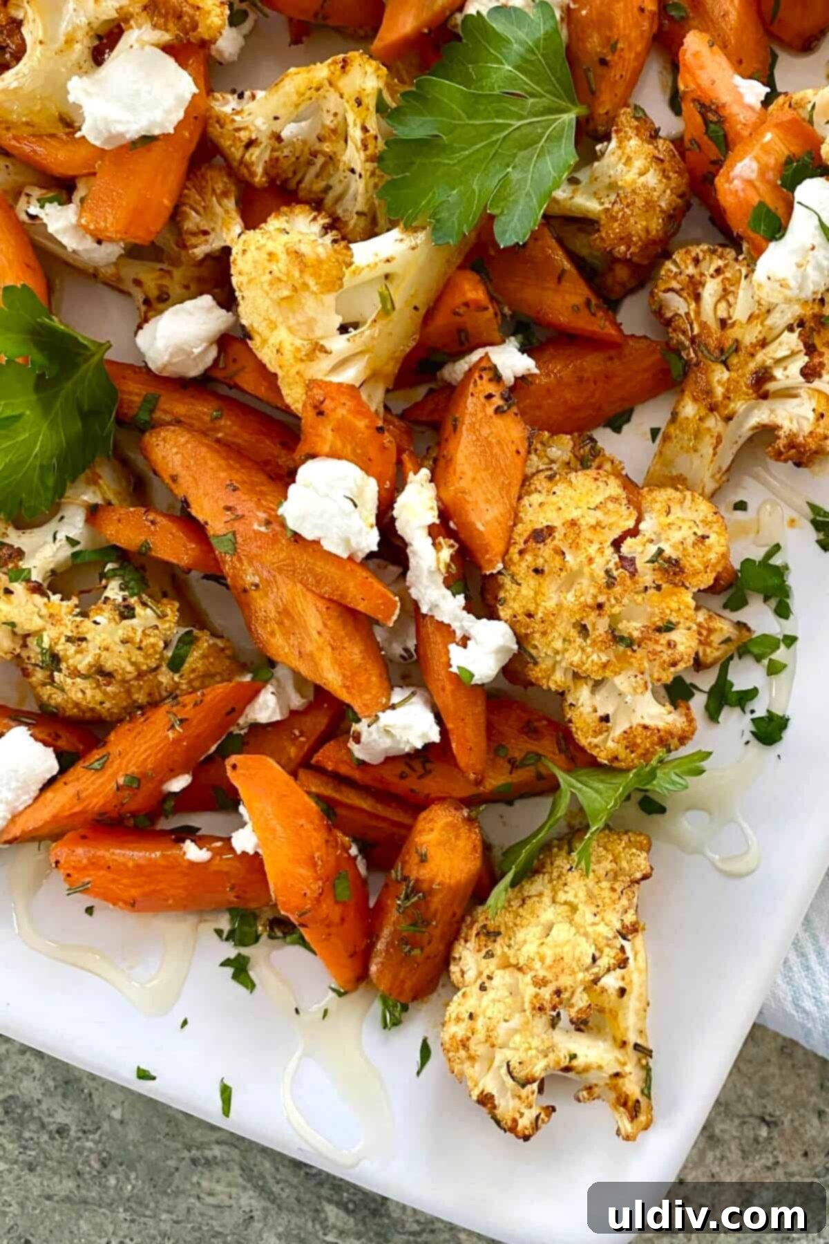 Honey-Glazed Roasted Carrots and Cauliflower with Tangy Goat Cheese 2 Roasted carrots and cauliflower with goat cheese on a white platter, garnished with fresh herbs.