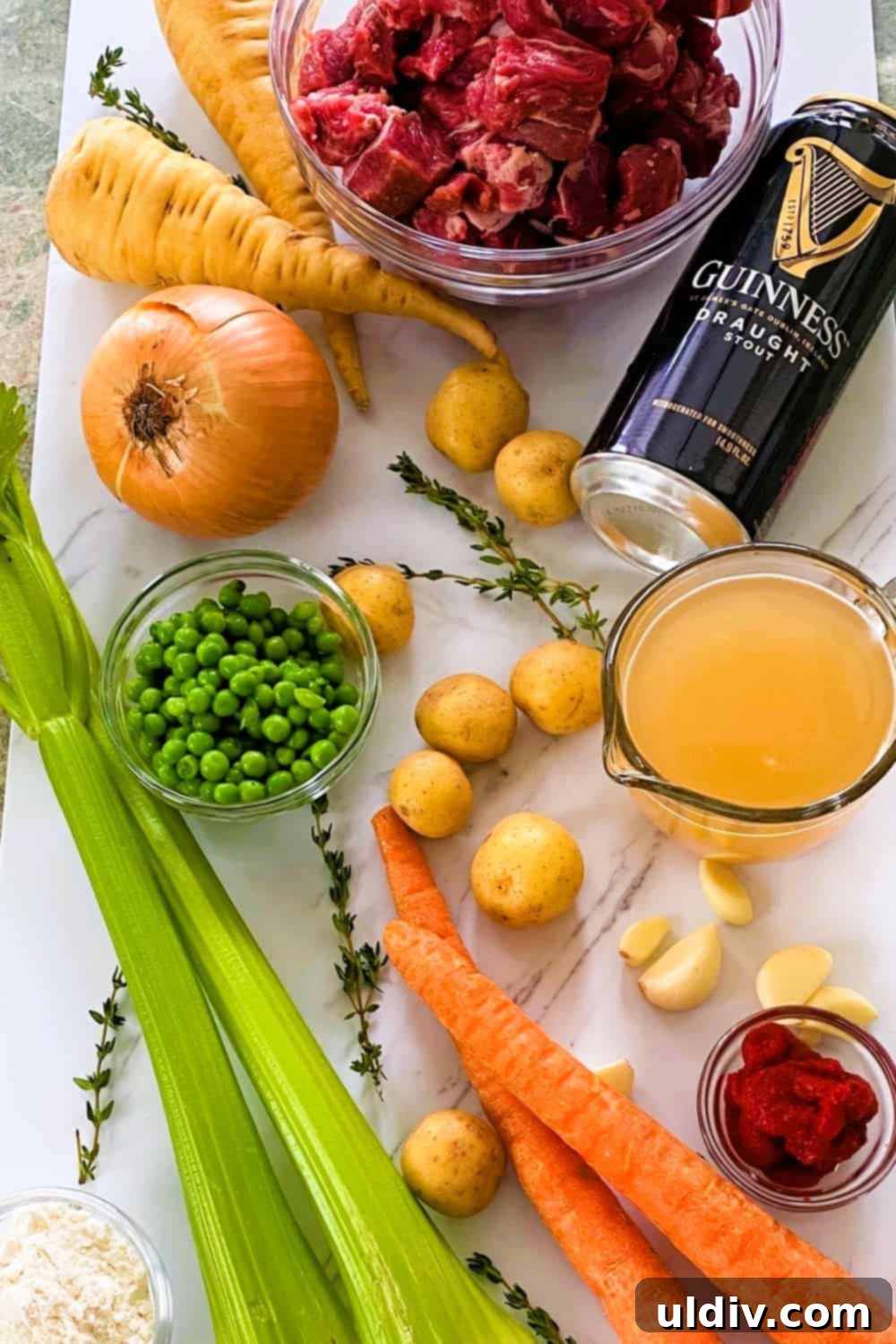 Hearty Guinness Lamb Stew 4 A flat lay of fresh ingredients for Irish stew: Guinness beer, frozen peas, whole potatoes, raw lamb shoulder chunks, a yellow onion, parsnips, and celery