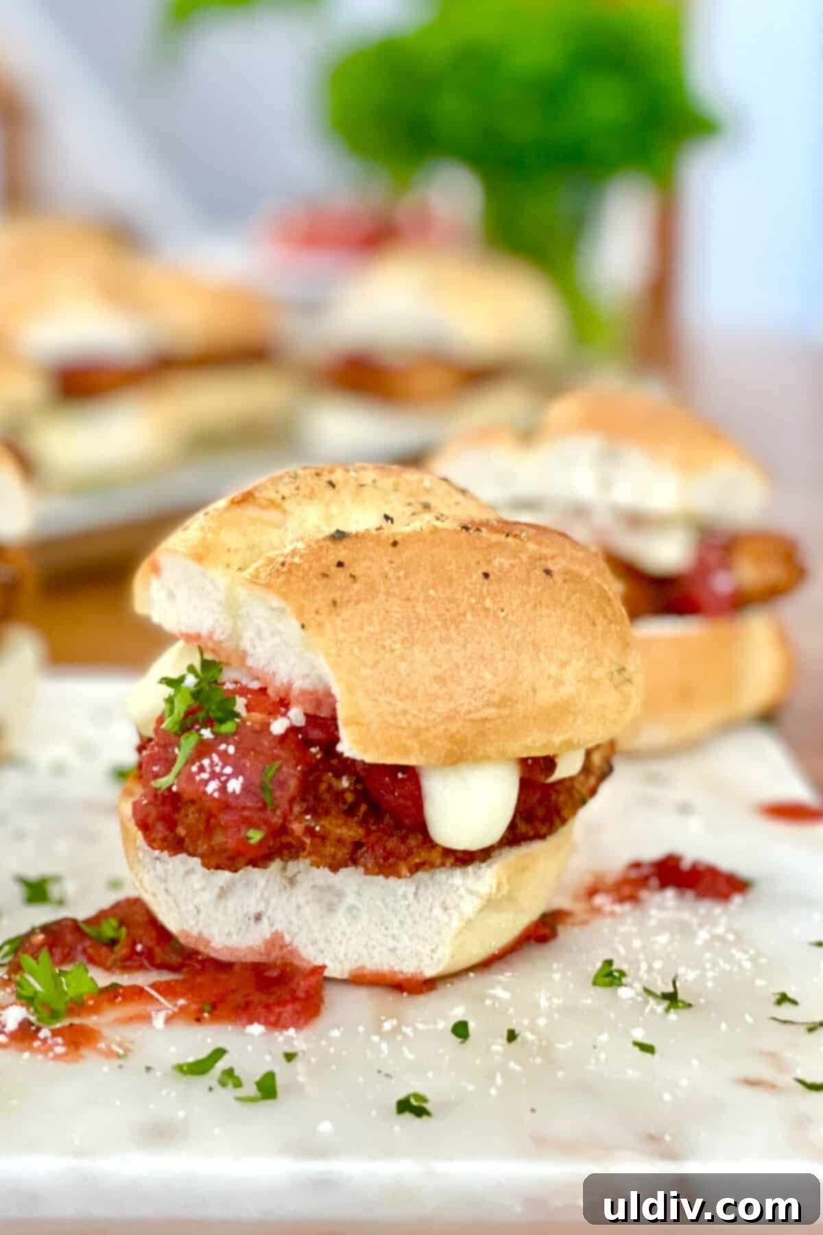 Bite-Sized Chicken Parm Sliders 8 A single mini chicken parm sandwich, perfectly assembled with a crispy chicken cutlet, melted mozzarella cheese, and rich marinara sauce, garnished with a fresh basil leaf.