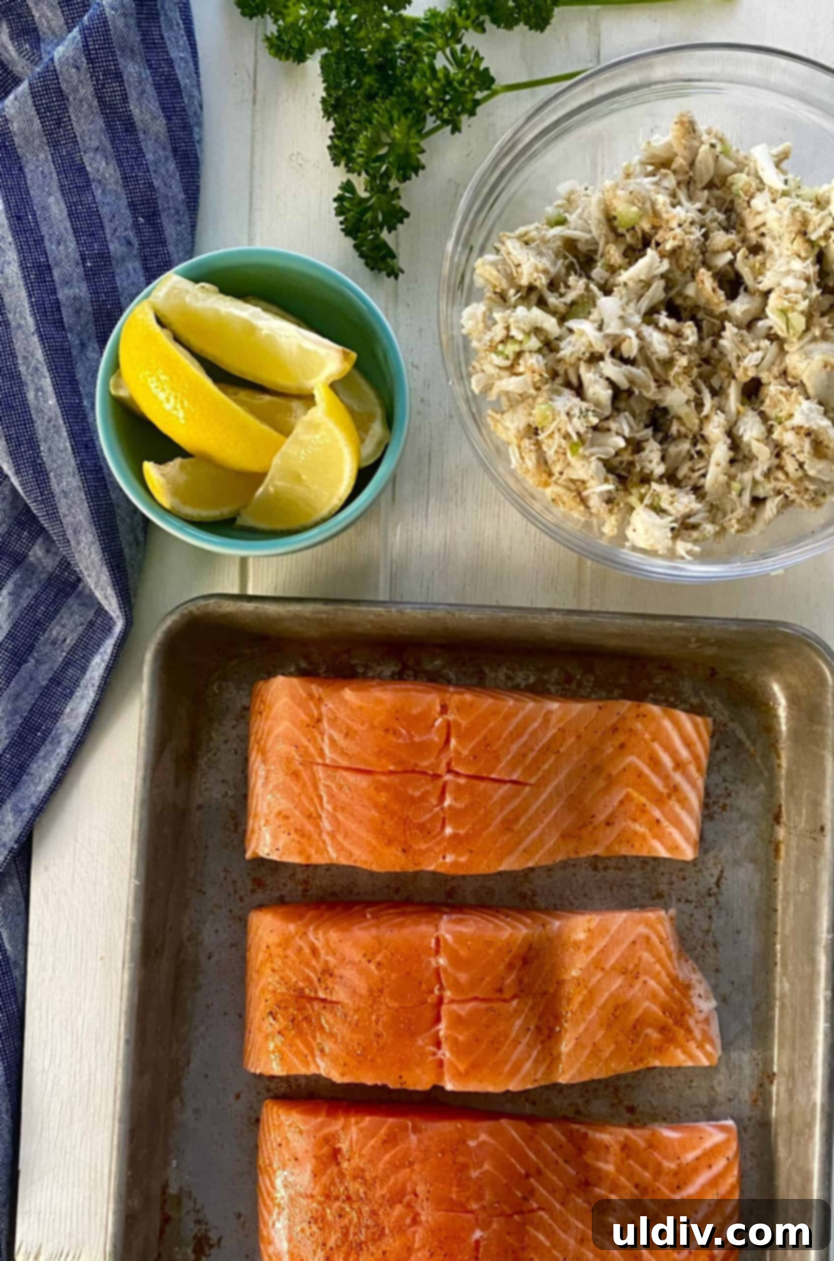 Crab-Filled Salmon Perfection 6 A bowl of delicious crab cake filling, fresh lemon halves, and uncooked salmon fillets with open pockets on a baking sheet, ready for assembly.