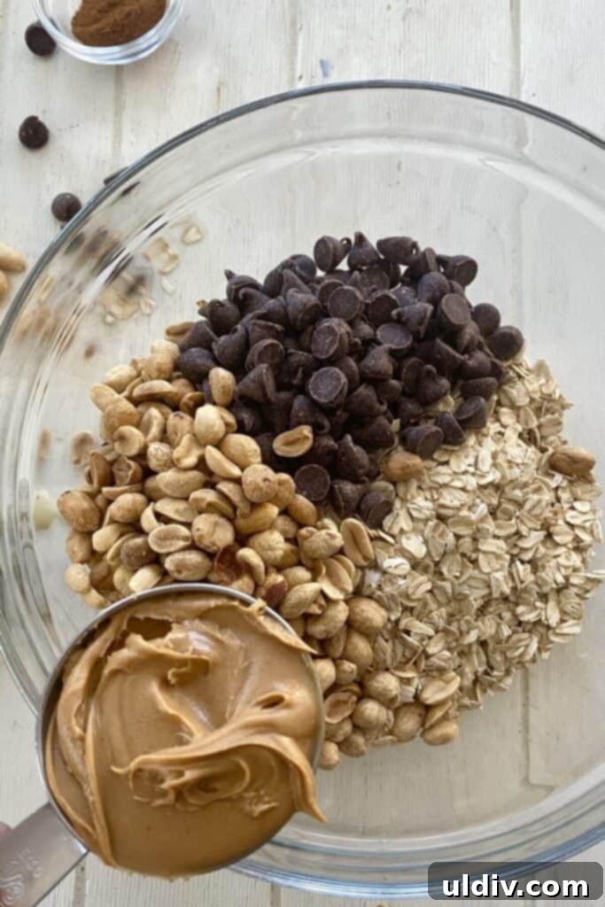 Scrumptious Peanut Butter Chocolate Chip Oat Bars 6 Adding creamy peanut butter to a bowl of oats, peanuts, and chocolate chips.