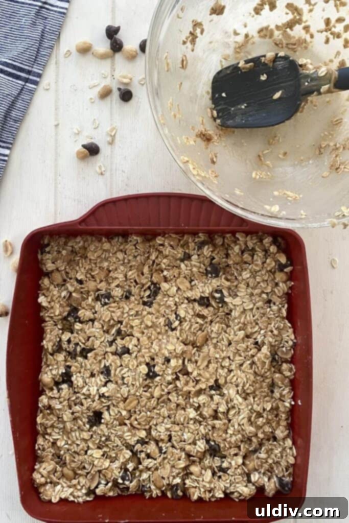 Chewy Chocolate Chip Peanut Butter Oat Bars 8 A spatula pressing the oat bar mixture evenly into a baking pan.