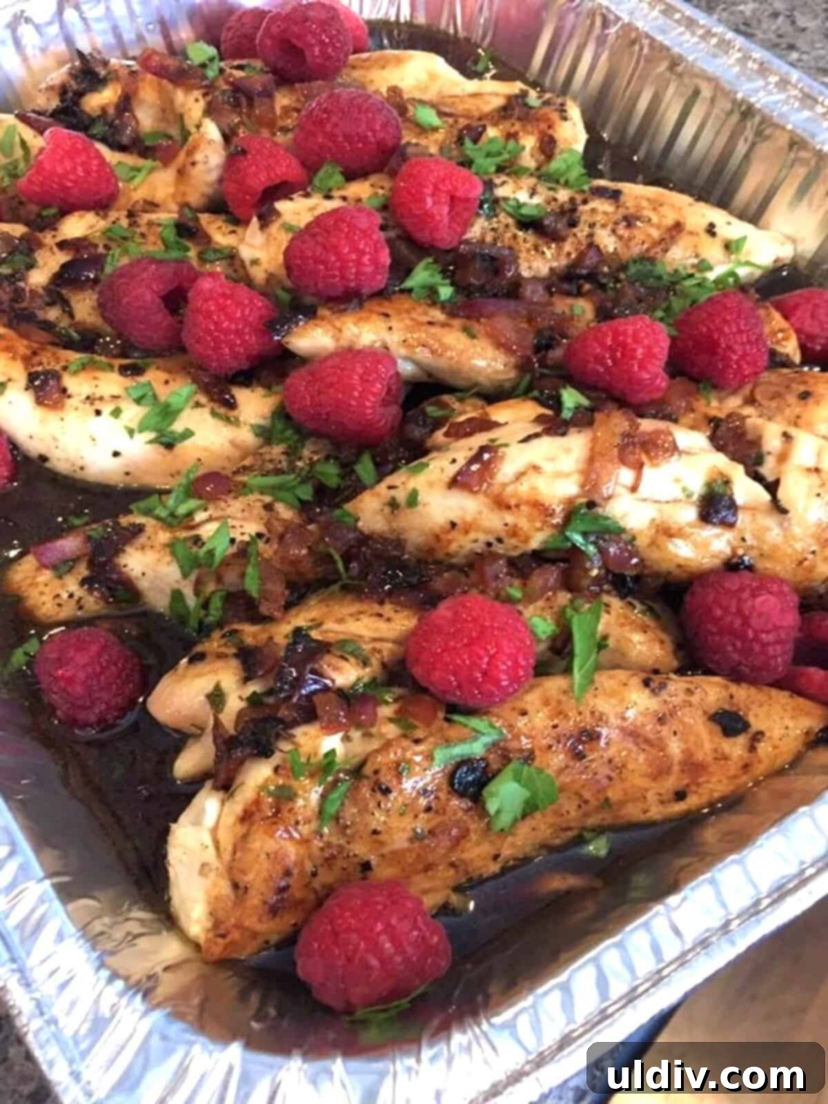 Raspberry Glazed Chicken with Almond Crunch 2 Foil pan filled with golden-brown raspberry balsamic chicken, garnished with fresh raspberries and toasted almonds.