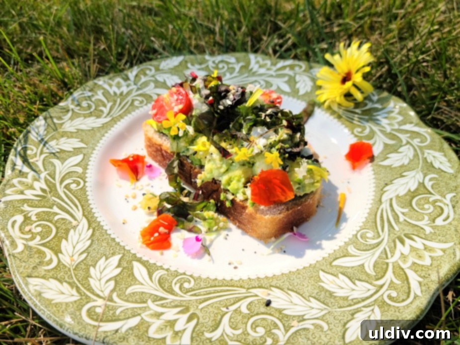 2024's Easiest Super Bowl Snacks 5 An open-faced sandwich on artisanal bread topped with creamy avocado, goat cheese, fresh Swiss chard, cherry tomatoes, chives, and a colorful assortment of edible flowers.