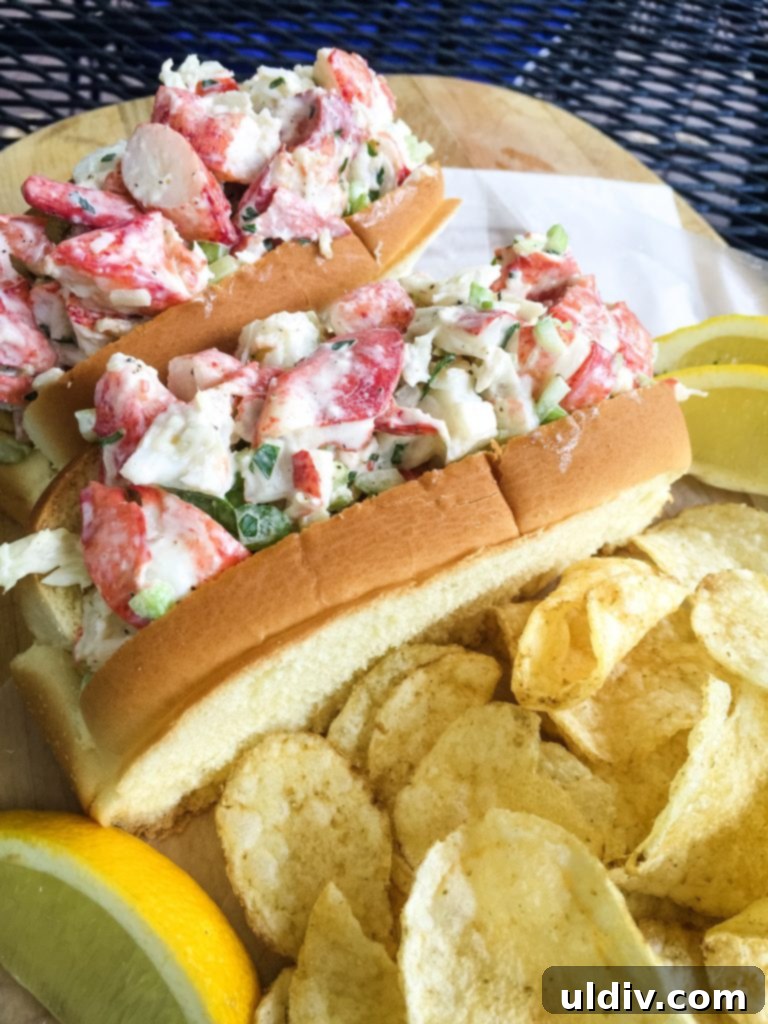 The Art of the Lobster Roll 4 Two exquisite cold lobster rolls, generously filled with fresh lobster salad, served alongside golden potato chips and bright lemon wedges, ready to be enjoyed.