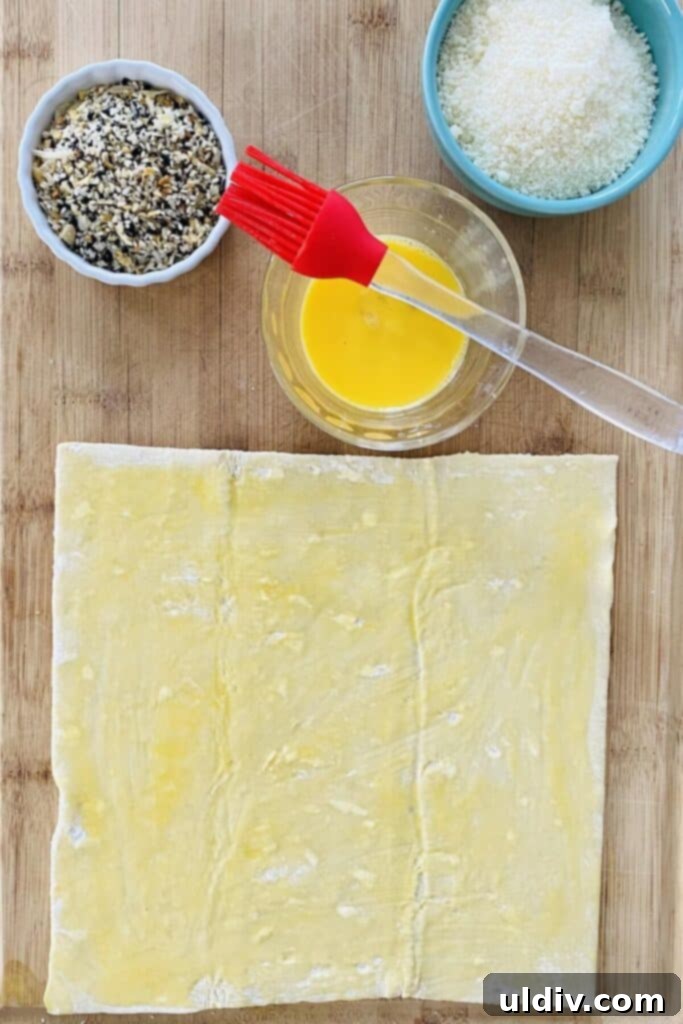 Crispy Everything Bagel Cheese Spirals 5 An unfolded puff pastry sheet brushed generously with egg wash, ready for seasoning.
